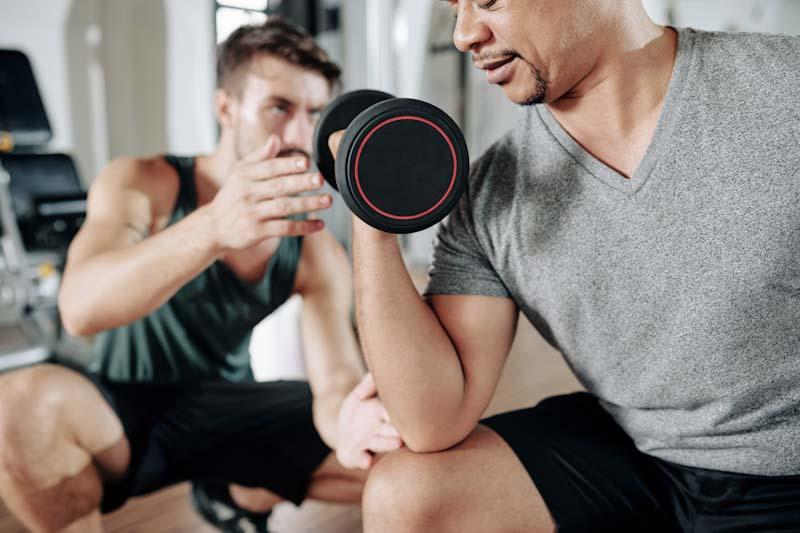 A certified personal trainer works with his client in the gym. Learn about managing your clients better with EliteTrainr.com.