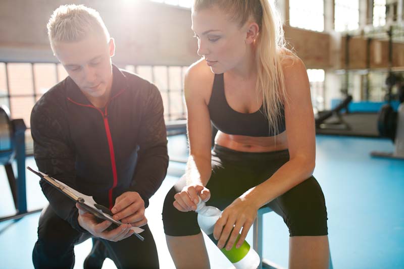 A personal trainer sits with a client to review a workout session in this file photo. Learn how to become a certified physical trainer at EliteTrainr.com.