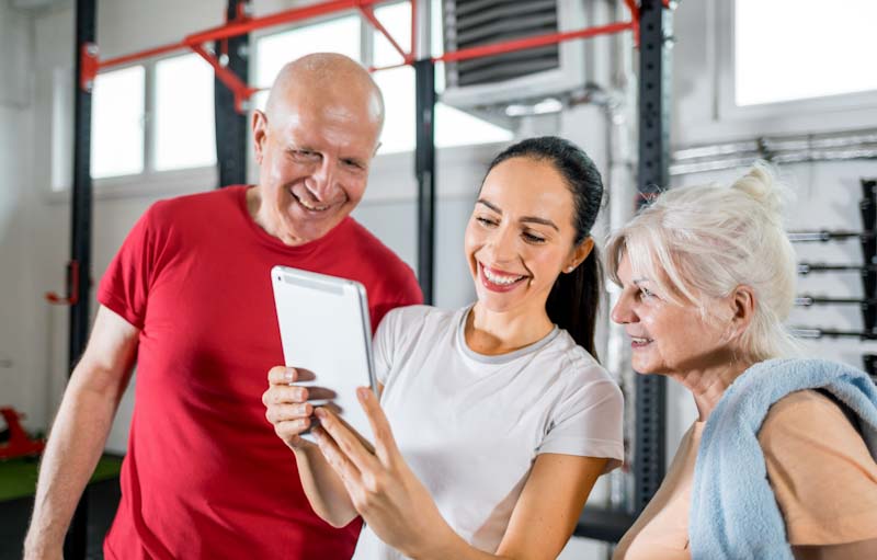 A personal trainer using Elite Trainr app on her tablet reviews results with a senior couple.