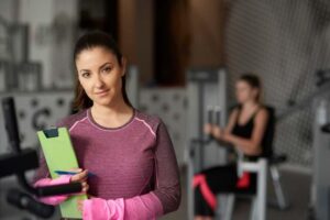 A personal trainer stands proudly holding a clipboard with her business plan for a personal training studio.