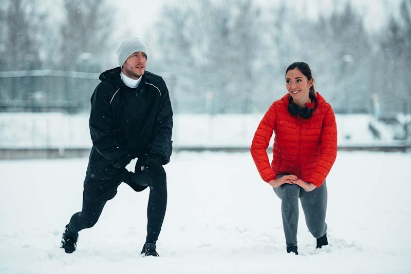 A couple stretches togher outside in winter. Learn the best winter workouts for your clients at EliteTrainr.com.