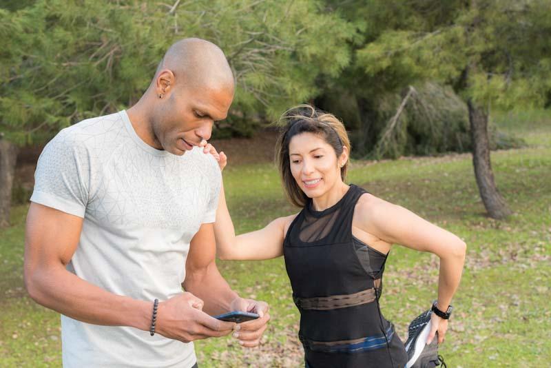 A personal trainer stands with his client setting up their account in the Elite Trainr app. Learn about personal trainer vs fitness coach and find out which career is for you at EliteTrainr.com.