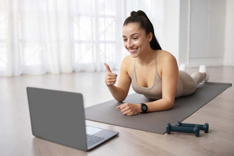 A woman happily greets her fitness coach online. Learn how you can become an online personal trainer at EliteTrainr.com.
