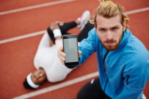 An athletic trainer holds up their white label featured fitness app on their smart device. Learn about fitness apps at EliteTrainr.com.