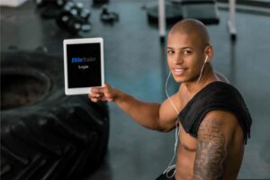 A trainer holds up a tablet with Elite Trainr, a fitness management app that includes online payment processing. Learn more at EliteTrainr.com.