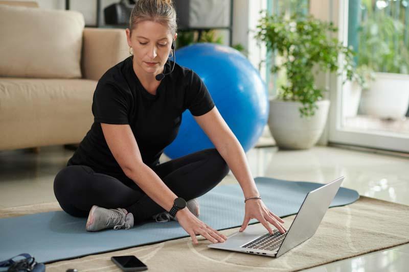 A personal trainer attends to her schedule using her laptop and smartphone. Learn about scaling your personal training business with digital tools at EliteTrainr.com.