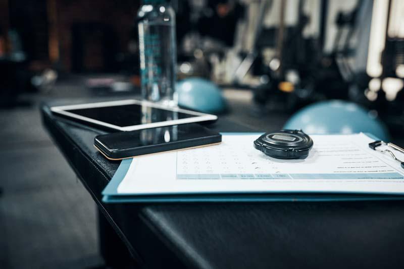 A tablet, smartphone, and stop watch are shown representing how technology helps scaling your personal training business. Learn more at EliteTrainr.com.