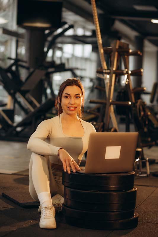 A new personal trainer is happy to use online fitness training management tools on her laptop. Learn how to train your clients online using Elite Trainr at EliteTrainr.com.
