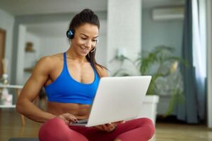 A new personal trainer works on her laptop with online fitness training management software. Learn more at EliteTrainr.com.